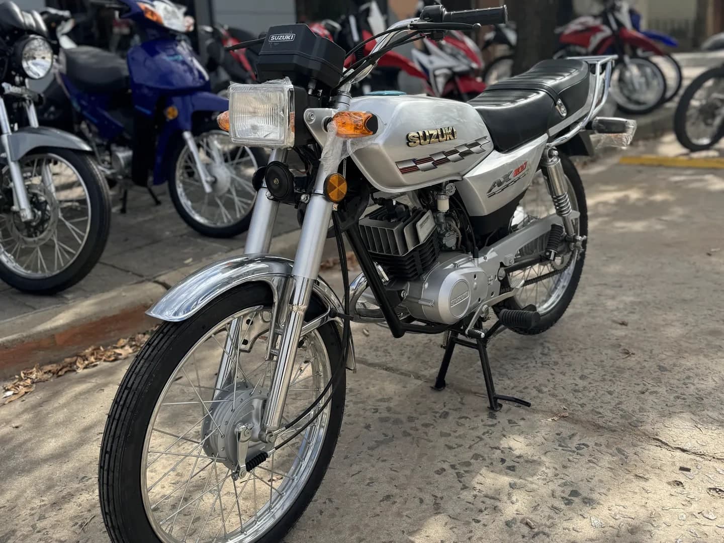 Suzuki AX 100 0 km blanca, vista lateral derecha en el salón de TodoMoto